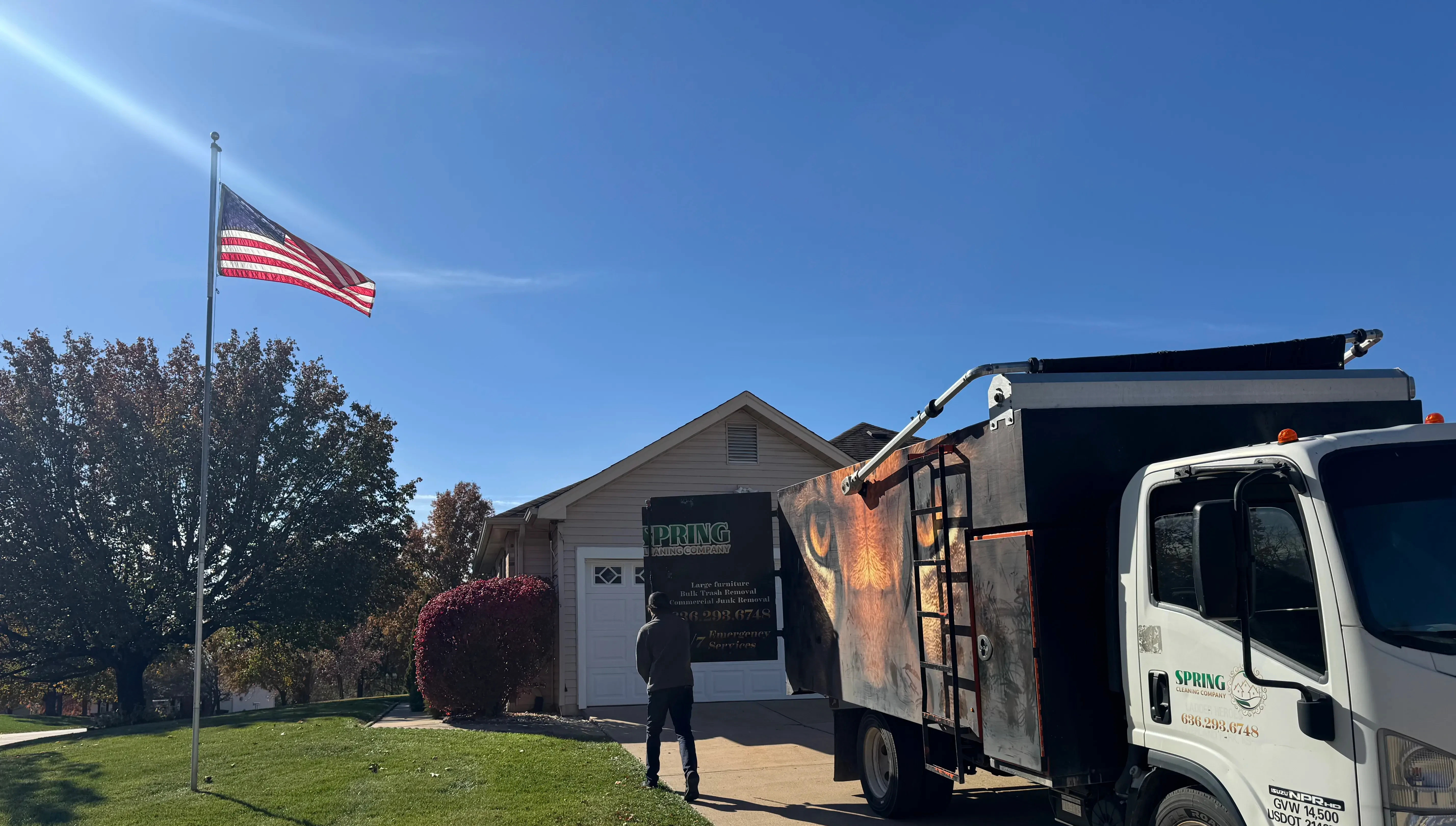 Spring Cleaning Company professional junk removal truck outside a residential property with a prominent american flag on the front lawn in St. Charles, Missouri