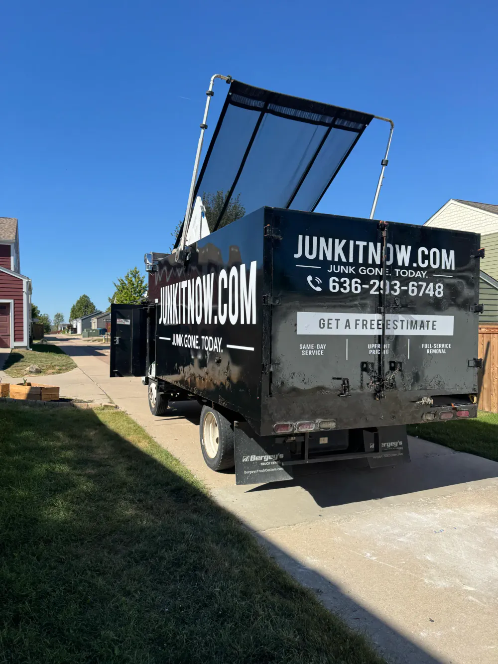 JunkItNow.com junk removal truck parked at a job site, rear doors showing the phone number and free estimate offer