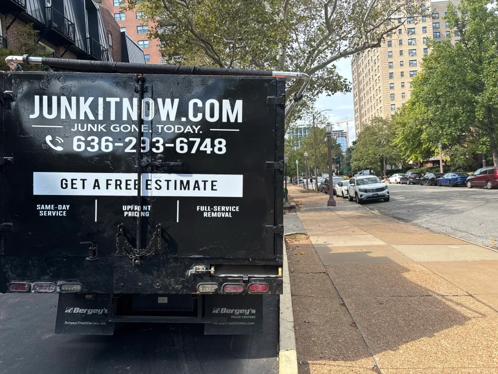 Rear of a JunkItNow.com junk removal truck on a city street, showing the phone number and free estimate offer